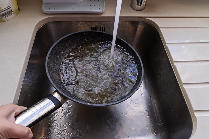 Frying pan with non-stick surface and hot oil under water tap flow in sink