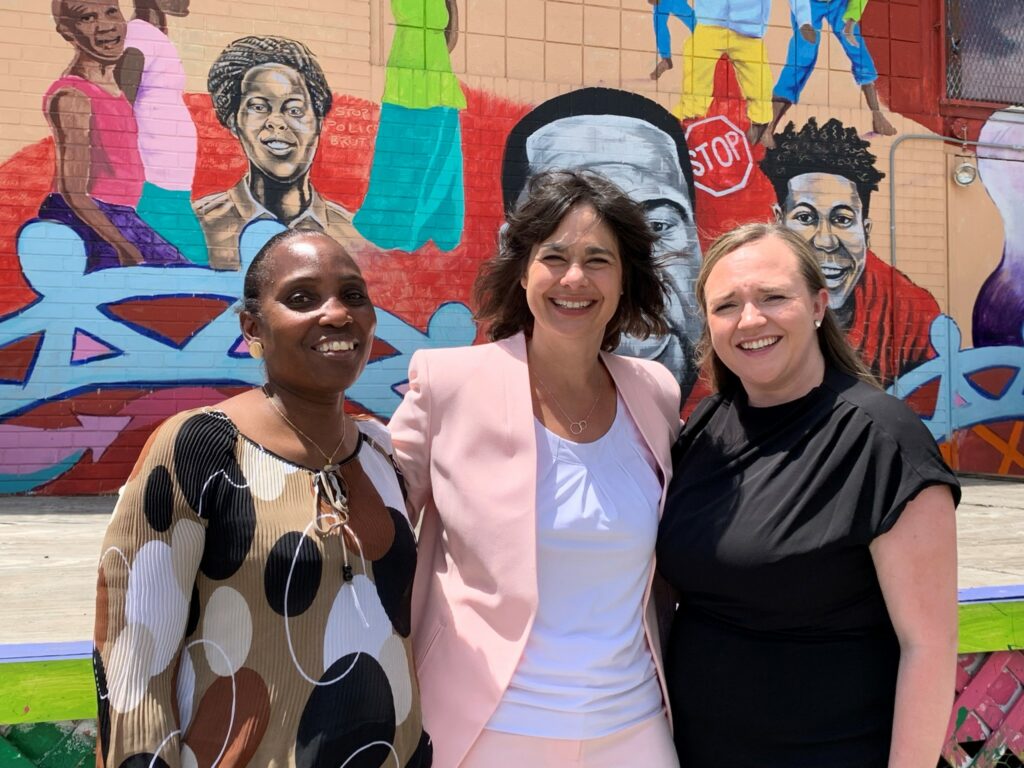 Three people in front of a mural outside