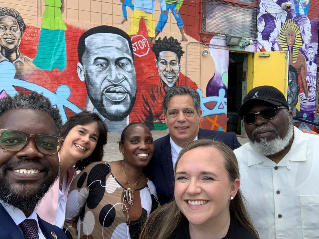 Group of people in front of a mural outside.