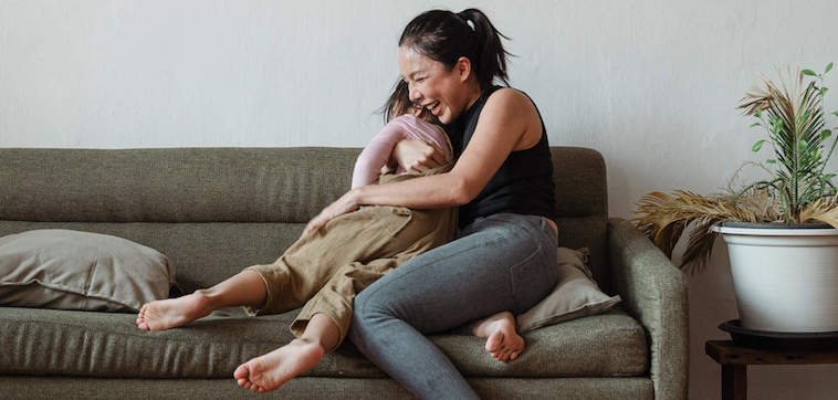 Women laughing while holding a child on a gray couch.
