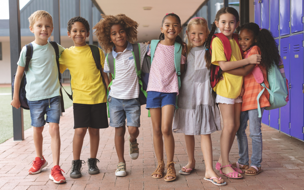 Seven children in a school hallway standing side by side.