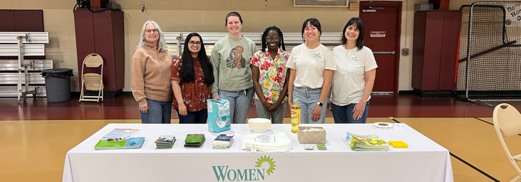 Six WHE staff members standing behind table of educational materials